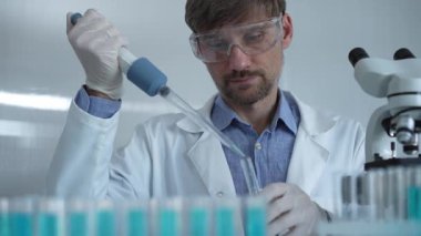 Laboratuvar önlüğü ve güvenlik gözlüğü takan bilim adamı deney tüpüne sıvı atmak için mikropipet kullanıyor. Portre görüntüsü. Tıp ve Bilim.