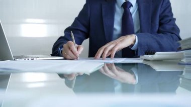 İş adamı hesap makinesi kullanıyor ve not alıyor. Ofis masasında dizüstü bilgisayar ve belgelerle çalışıyor. İş dünyasında denetim ve vergi teması.