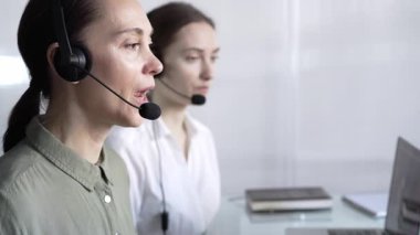 Mavi günlük bluzlu odaklı kadın çağrı merkezi operatörü müşterilerine çevrimiçi olarak yardım ediyor, müşteri desteği sağlıyor ve sorulara cevap veriyor. Çağrı merkezi operatörleri