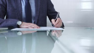 Çağdaş bir ofis ortamında modern cam bir masanın üzerinde profesyonel giyimli bir işadamı kalemle kontrat imzalıyor. İş adamları veya denetim kavramı