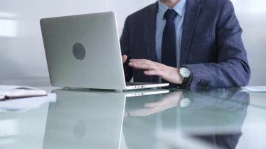 Mavi ceket giyen işadamı, modern bir ofisteki cam bir masadaki dizüstü bilgisayarla çevrimiçi iletişime odaklanarak üretkenlik ve konsantrasyon gösteriyor. İş veya denetim kavramı.