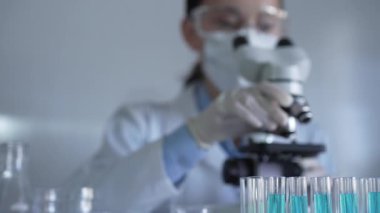 Laboratuvar tüpleri odaklandı, yakın görüş. Kadın araştırmacı, arka planda mikroskop kullanıyor. Tıp ve bilim konsepti.
