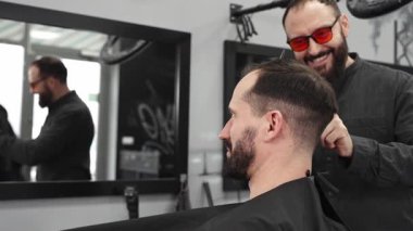 Profesyonel berber, modaya uygun bir berber dükkanında profesyonel bir makasla müşterinin saçını kesiyor, şık ve modern bir saç kesimi yapıyor, aynı zamanda rahat bir tımar deneyimi sağlıyor.