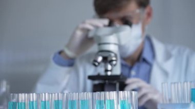 Laboratuvar tüpleri odaklandı, yakın görüş. Beyaz koruyucu eldivenli bilim adamı araştırmacı arka planda mikroskop kullanıyor. Tıp ve bilim konsepti.