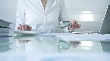 İş kadını, mali verileri büyüteç ve hesap makinesiyle analiz ediyor, muhasebe ve denetleme görevlerini yerine getiriyor. İş dünyasında denetim ve vergi teması.