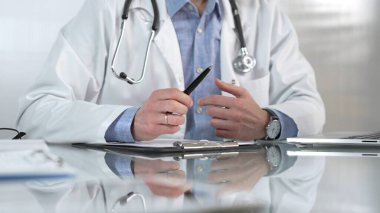 Mavi gömlek, steteskop ve laboratuvar önlüğü giyen erkek doktor, cam bir masadaki hastaya dizüstü bilgisayarla teşhisi açıklarken elleriyle hareket ediyor. Tıp konsepti.