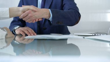 İş adamları toplantıda anlaşmaya vardıktan sonra cam masada el sıkışıyorlar. Tokalaşmanın yakın çekimi.