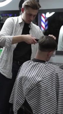 Profesyonel berber müşterilerin saçlarını elektrikli makasla dikkatlice buduyor, modern bir berber dükkanında şık ve kusursuz bir saç kesimi sağlıyor.