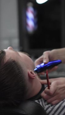 Profesyonel berber, erkek müşterinin boynundaki kılları elektrikli makasla dikkatlice buduyor ve modern berber dükkanında titiz bir bakım hizmeti sunuyor.