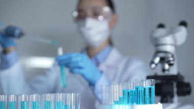 Laboratuvar tüpleri odaklandı, yakın görüş. Kadın araştırmacı, arka planda bir mikro pipet kullanıyor. Tıp ve Bilim.