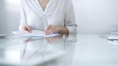 Beyaz noktalı bluzlu iş kadını, cam bir masada güncel ofis ortamında evrakları tutarken evrak işleriyle uğraşıyor. İş adamları konsepti.