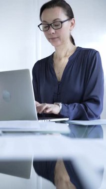 İyi aydınlatılmış ofisteki modern cam masada dizüstü bilgisayarda yazan odaklanmış iş kadını. İş adamları konsepti.