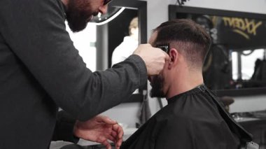 Moda bir berber dükkanında elektrikli jiletle saç kesen profesyonel berber, şık ve modern bir saç kesimi yaparken aynı zamanda rahat bir tımar deneyimi sağlıyor.