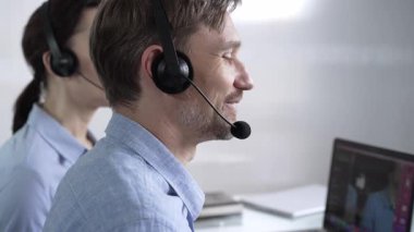 Mavi günlük gömlekli odaklı erkek çağrı merkezi operatörü müşterilerine çevrimiçi olarak yardım ediyor, müşteri desteği sağlıyor ve sorulara cevap veriyor. Çağrı merkezi operatörleri