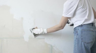 Meçhul inşaat işçisi duvara alçı uygulamak için macun bıçağı kullanıyor, kusurları doldurarak ve pürüzsüz bir yüzey yaratarak, yakın çekim görüntüsü oluşturarak ev yenileme ve iyileştirme yapıyor.