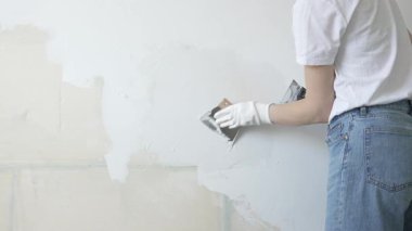 Meçhul inşaat işçisi duvara alçı uygulamak için macun bıçağı kullanıyor, kusurları doldurarak ve pürüzsüz bir yüzey yaratarak, yakın çekim görüntüsü oluşturarak ev yenileme ve iyileştirme yapıyor.