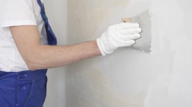 Bilinmeyen inşaat işçisi, beyaz duvar boyuyor, mavi tulum giyiyor ve apartman yenileme projesi sırasında koruyucu beyaz eldivenler giyiyor..