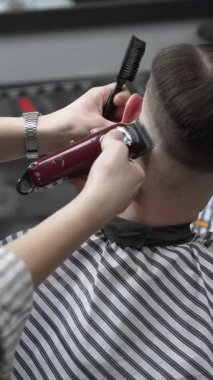 Profesyonel berber müşterilerin saçlarını elektrikli makasla dikkatlice buduyor, modern bir berber dükkanında şık ve kusursuz bir saç kesimi sağlıyor.