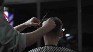 Profesyonel berber erkek müşterinin saçını şık bir berber dükkanında makas ve tarak kullanarak ustaca kesiyor ve arka planda belirgin bir şekilde berber direği sergiliyor.