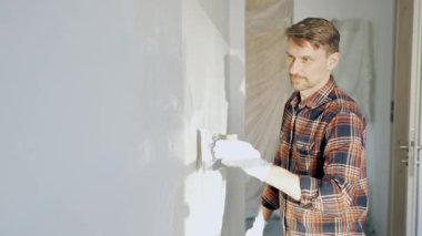 Eldiven giyen erkek inşaat işçisi, bir el aleti kullanarak duvara alçı yapıştırıyor, ev yenileme veya inşaat projesine katkıda bulunuyor