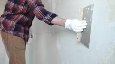 Meçhul erkek inşaat işçisi, eldivenleri titizlikle takıyor. Duvarı alçılamak için bıçak kullanıyor. Ev yenileme projesinde ustalıkla yüzeyi düzleştiriyor.