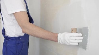 Bilinmeyen inşaat işçisi, beyaz duvar boyuyor, mavi tulum giyiyor ve apartman yenileme projesi sırasında koruyucu beyaz eldivenler giyiyor..