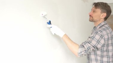 Profesyonel erkek ressam apartman duvarına beyaz boya sürüyor. Kapsamlı ev yenileme çalışmaları sırasında iç mekanı sürekli darbelerle değiştiriyor..