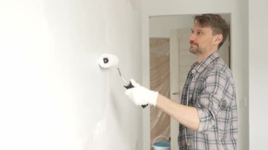 Profesyonel erkek ressam apartman duvarına beyaz boya sürüyor. Kapsamlı ev yenileme çalışmaları sırasında iç mekanı sürekli darbelerle değiştiriyor..
