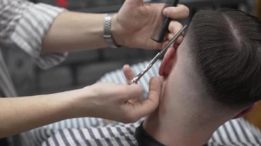 Profesyonel berber, müşterilerin saçlarını buduyor, makas ve tarakla kusursuz bir solukluk çiziyor, çağdaş berber dükkânı düzenliyor, uzman tımar ediyor.