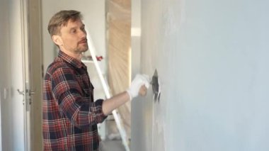 Eldiven giyen erkek inşaat işçisi, bir el aleti kullanarak duvara alçı yapıştırıyor, ev yenileme veya inşaat projesine katkıda bulunuyor