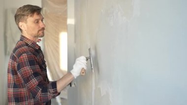 Eldiven giyen erkek inşaat işçisi, macun bıçağıyla ustalıkla duvara alçı yapıştırıyor, bir ev yenileme projesiyle meşgul, iç mekanı hassasiyetle büyütüyor.