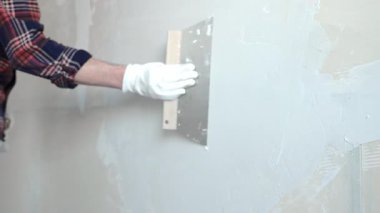 Meçhul erkek inşaat işçisi, eldivenleri titizlikle takıyor. Duvarı alçılamak için bıçak kullanıyor. Ev yenileme projesinde ustalıkla yüzeyi düzleştiriyor.