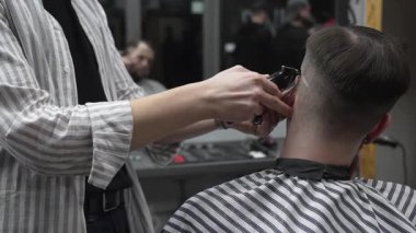 Profesyonel berber müşterilerin saçlarını elektrikli makasla dikkatlice buduyor, modern bir berber dükkanında şık ve kusursuz bir saç kesimi sağlıyor.