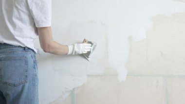 Meçhul inşaat işçisi duvara alçı uygulamak için macun bıçağı kullanıyor, kusurları doldurarak ve pürüzsüz bir yüzey yaratarak, yakın çekim görüntüsü oluşturarak ev yenileme ve iyileştirme yapıyor.
