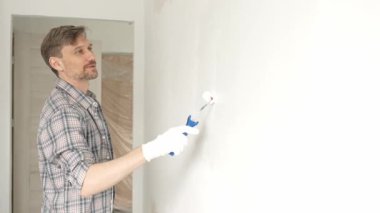 Profesyonel erkek ressam apartman duvarına beyaz boya sürüyor. Kapsamlı ev yenileme çalışmaları sırasında iç mekanı sürekli darbelerle değiştiriyor..