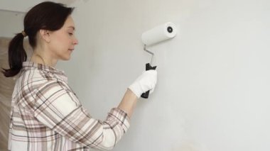 Profesyonel bir ressam koruyucu eldivenler giyerek duvarda pürüzsüz bir şekilde beyaz boya sürüyor, evin içini kusursuz bir fırça ve titiz bir boya tekniğiyle yeniliyor.