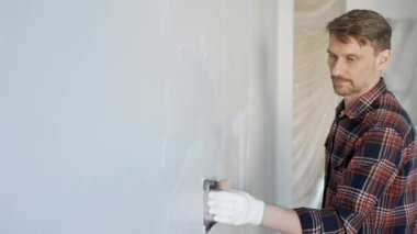 Eldiven giyen erkek inşaat işçisi, bir el aleti kullanarak duvara alçı yapıştırıyor, ev yenileme veya inşaat projesine katkıda bulunuyor