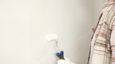 Eldivenli bir eli boya silindiri kullanarak kapamak, duvara yeni bir kat beyaz boya sürmek, bir ev yenileme projesi sırasında temiz ve eşit bir yüzey yaratmak