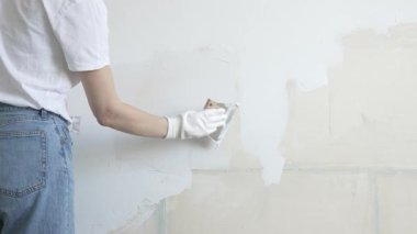 Meçhul inşaat işçisi duvara alçı uygulamak için macun bıçağı kullanıyor, kusurları doldurarak ve pürüzsüz bir yüzey yaratarak, yakın çekim görüntüsü oluşturarak ev yenileme ve iyileştirme yapıyor.