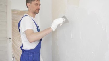 Profesyonel inşaat işçisi mavi tulum ve beyaz eldiven giyerek bir daireye beyaz bir duvar örüyor.