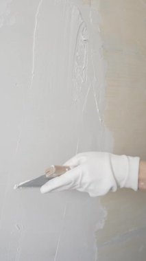 Kadın duvara macun bıçağıyla alçı yapıştırıyor, koruma için eldiven takıyor ve ev tadilatı, dikey görünüm süresince pürüzsüz ve pürüzsüz bir şekilde bitmesini sağlıyor.