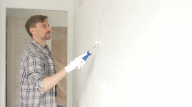 Orta yaşlı bir adam, apartman duvarında küçük bir silindirle beyaz boya yuvarlıyor. Geniş kapsamlı ev yenileme çalışmaları sırasında sürekli darbeler alarak iç mekanı değiştiriyor..