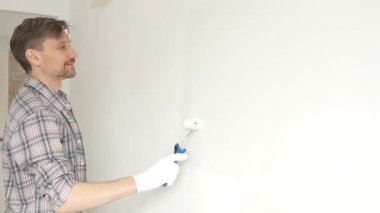 Orta yaşlı bir adam, apartman duvarında küçük bir silindirle beyaz boya yuvarlıyor. Geniş kapsamlı ev yenileme çalışmaları sırasında sürekli darbeler alarak iç mekanı değiştiriyor..