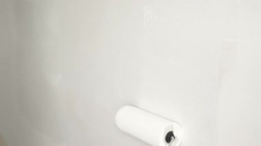 Eldivenli bir eli boya silindiri kullanarak kapamak, duvara yeni bir kat beyaz boya sürmek, bir ev yenileme projesi sırasında temiz ve eşit bir yüzey yaratmak