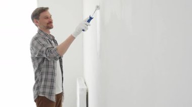 Profesyonel ressam iç duvarda beyaz boya yuvarlıyor, dikkatlice yüzeyini pürüzsüz bir şekilde kaplıyor, hatta ev yenileme projesi sırasında darbeler alıyor, kusursuz resim tekniğini vurguluyor.