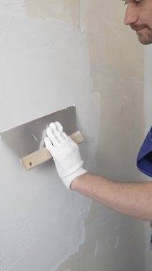 Profesyonel inşaat işçisi mavi tulum ve beyaz eldiven giyerek, yenilenmiş, dikey görünümlü bir apartman dairesine beyaz bir duvar örmek için mala kullanıyor.