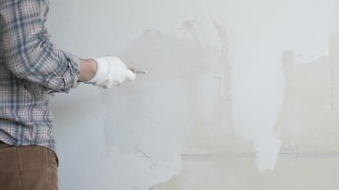 Meçhul inşaat işçisi duvara alçı uygulamak için macun bıçağı kullanıyor, kusurları doldurarak ve pürüzsüz bir yüzey yaratarak, yakın çekim görüntüsü oluşturarak ev yenileme ve iyileştirme yapıyor.