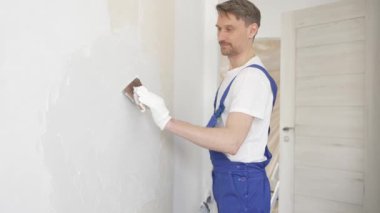 Profesyonel inşaat işçisi mavi tulum ve beyaz eldiven giyerek bir daireye beyaz bir duvar örüyor.