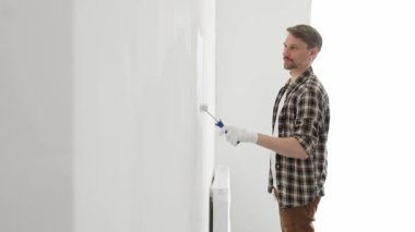 Profesyonel ressam beyaz duvarı silindirle düzleştiriyor, ev dekorasyonu sırasında koruyucu eldiven takıyor, iç mekanı yeni boyama tekniğiyle değiştiriyor.
