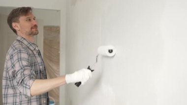 Profesyonel erkek ressam apartman duvarına beyaz boya sürüyor. Kapsamlı ev yenileme çalışmaları sırasında iç mekanı sürekli darbelerle değiştiriyor..